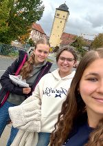 Unsere Lehrerin Fr. Flucher und die beiden Schülerinnen posieren für ein Selfie vor einem historischen Gebäude.