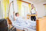 Patient im Krankenbett liegend bekommt von Schülerin, welche die Ausbildung zur Heimhelferin macht, das Frühstück.