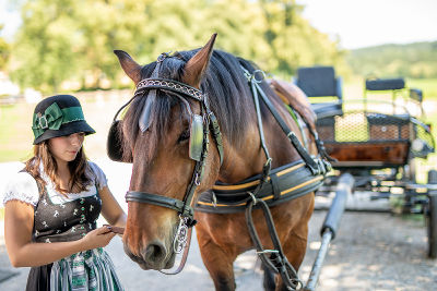 Reiterin im Dirndl neben einem Pferd, das sie am Halfter hält