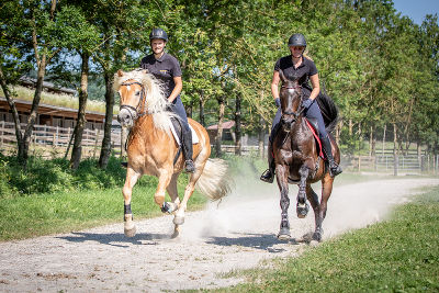 Zwei Schülerinnen sind reitend auf einem Pferd unterwegs