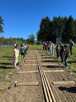 Schüler*innen stehen an Beeten und freuen sich schon die erste Pflanze hineinzusetzen. 