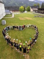 Gruppe von SchülerInnen bildet ein Herz auf einer Wiese vor dem Schulgebäude.