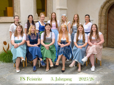 Gruppe junger Menschen in traditioneller steirischer Tracht posiert vor einem Gebäude.
