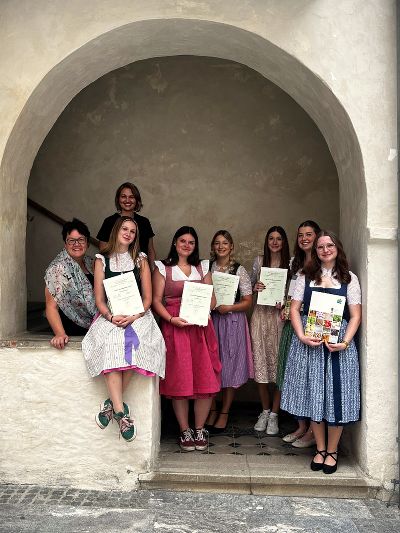 Gruppe in traditioneller Tracht vor einem historischen Gebäude. Menschen stehen und sitzen lächelnd für ein Gruppenfoto.