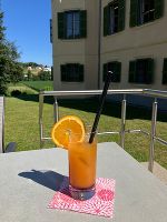 Der Mocktail steht auf dem Tisch schön angerichtet in einem Glas, welches mit einer Orange garniert wurde. Im Hintergrund sieht man das Schloss.