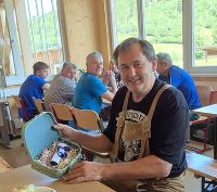 Roman Wilfing sitzt an einem Tisch mit einem Geschenk. Im Hintergrund sind weitere Personen in einem hellen Raum zu sehen.
