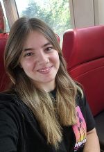 Junge Frau mit lächelndem Gesicht und langen Haaren auf einem Transportmittel. Rote Sitze im Hintergrund.