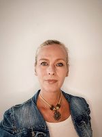 Person mit blonden Haaren und Jeansjacke vor hellem Hintergrund. Blick in die Kamera. Porträt-Aufnahme.