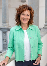 Frau mit rötlichen Locken, grüner Jacke vor hellgrauem Hintergrund
