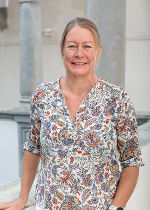 Eine Dame mit blonden halblangem Haar und eeiner bunten Bluse.