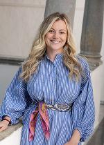 Junge Dame mit blond gelocktem Haar und einem blau weiß gestreiftem Kleid vor grauem Hintergrund