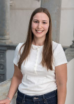 Junge Dame mit langen brünetten Haaren und weißem Shirt vor grauem Hintergrund