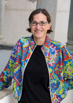 Dame mit kurzen dunklen Haaren und einer schmalen Brille in einer olivfarbenen Bluse vor einer Säule stehend.