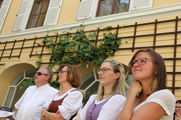 Ein männlicher und vier weibliche Absolventen sitzen im Schlosshof im Sommer