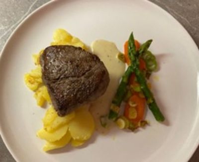 Rindersteak auf Erdäpfelgröstl mit glasierten Karotten und Spargel auf einem weißen Teller