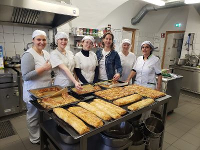 Schülerinnen, Lehrerinnen und Küchenpersonal stehen hinter einem Tisch auf dem mehrere Backbleche mit dem fertigen Gemüsewinterstrudel gemessen werden. Schülerinnen, Lehrerinnen und Küchenpersonal stehen hinter einem Tisch auf dem mehrere Backbleche mit dem fertigen Gemüsewinterstrudel gemessen werden.