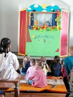 Das bunt dekoriert Kasperltheater, davor sitzen Kinder auf Langbänken.