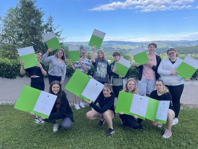 Schüler:innen der Fachschule Burgstall stehen in der Wiese und halten ihre Diplome Office-Assistent des Wifi Steiermark in den Händen.